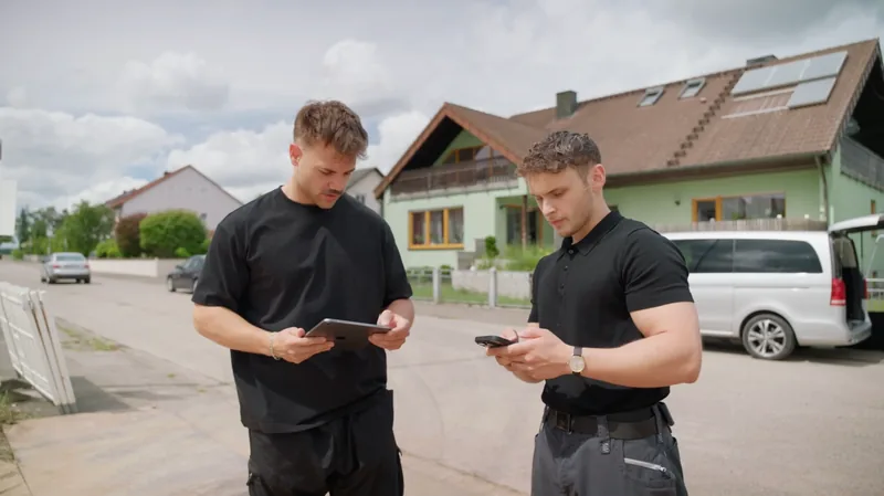 Zwei Männer arbeiten auf der Straße vor einem Wohnhaus mit Tablet und Smartphone