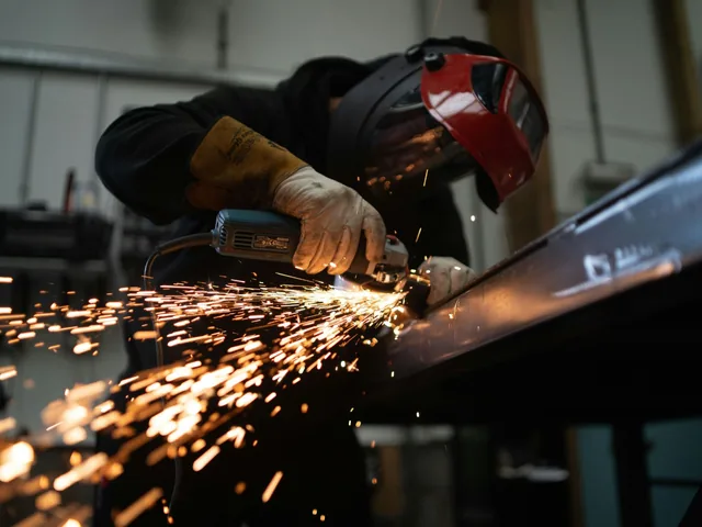 Metallbauer mit Schweißhelm schleift Stahl, Funken fliegen