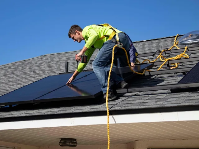 Monteur in Sicherheitsgurt montiert ein Solarmodul auf einem Dach